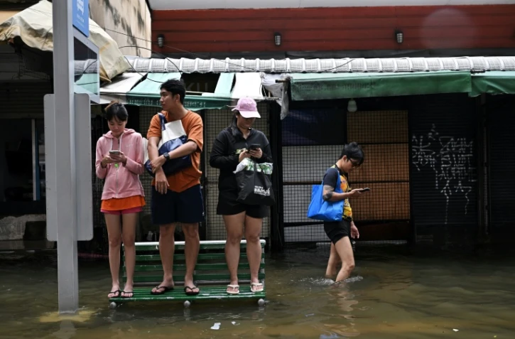 Des habitants sur un banc dans une rue de Bangkok, où l'état de catastrophe naturelle a été déclaré après des pluies diluviennes qui ont inondé habitations, commerces et axes de circulation, le 27 septembre 2026