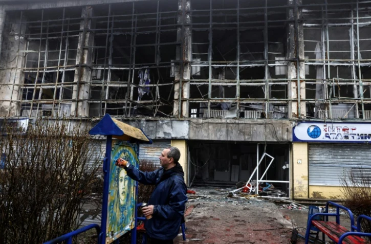 L'artiste français Christian Guémy, alias C215, peint une de ses oeuvres sur un panneau près d'une station de métro et d'un marché alimentaire gravement endommagés par les frappes russes sur Kiev, le 1er avril 2022