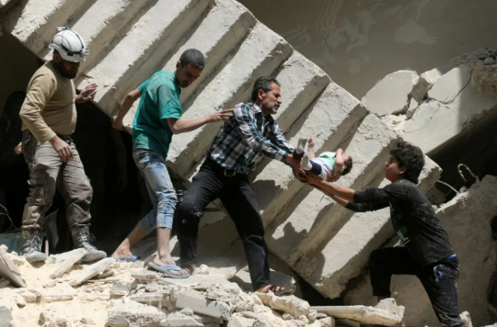 Des volontaires de la Défense civile syrienne, sortent un enfant des décombres d'un immeuble bombardé à Alep le 28 avril 2016