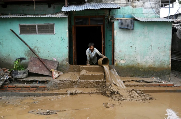 Un homme nettoie la boue devant sa maison, dans une zone touchée par les inondations à Katmandou, le 29 septembre 2024
