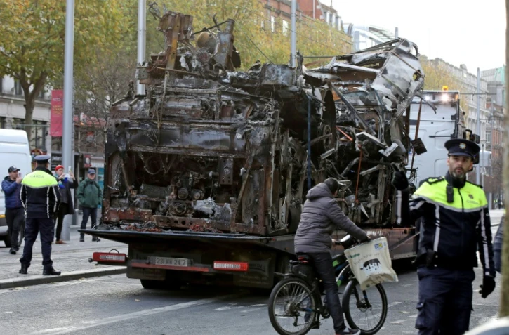 La carcasse d'un bus incendié est évacuée d'une rue de Dublin le 24 novembre 2023 au lendemain d'émeutes imputées à l'extrême droite