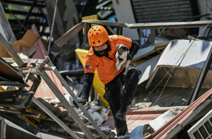 Un secouriste porte un chien de sauvetage lors d'opérations de recherche au niveau d'un bâtiment effondré, le 9 juin 2026 à General Santos aux Philippines