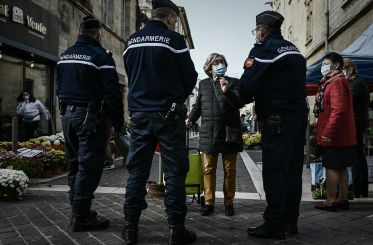 Une femme portant un masque de protection discute avec des gendarmes à l'entrée d'un marché à Libourne, le 30 octobre 2020