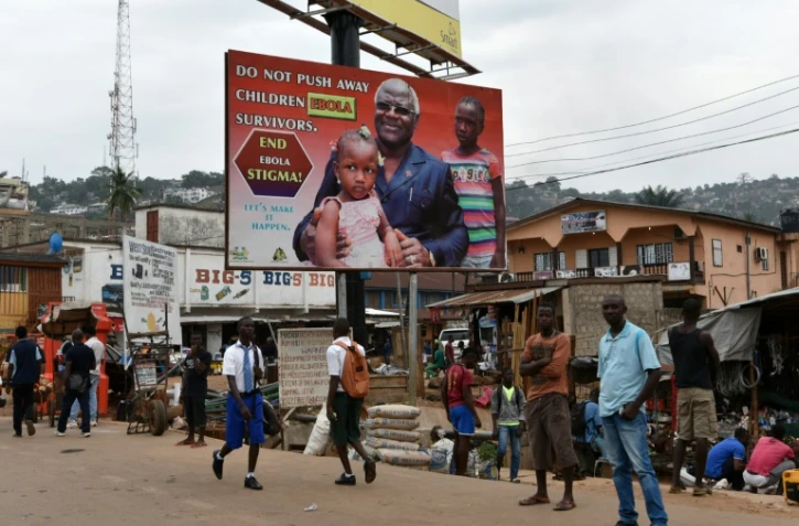 Des habitants de Freetown en Sierra Leone marchent sous une affiche de campagne contre Ebola représentant le président Ernest Bai Koroma