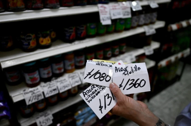 Paola Basso, qui tient une supérette à Moron, dans la banlieue de Buenos Aires, montre des étiquettes d'anciens prix, le 22 novembre 2023