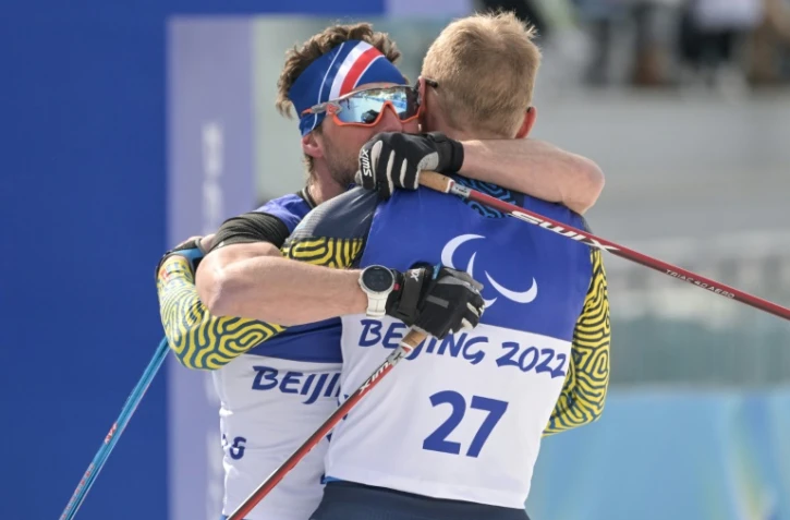 Le fondeur français Benjamin Daviet (g), médaillé d'or en sprint debout enlace l'Ukrainien Grygorii Vovchynskyi (3e), aux Jeux paralympiques de Pékin, le 9 mars 2022