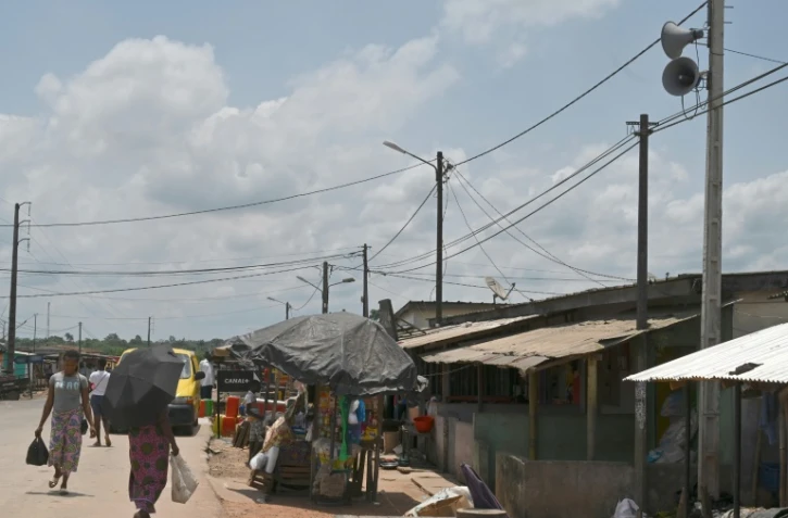 Des habitants font leurs courses dans une rue du village d'Azaguié Ahoua, près d'Abidjan, où des hauts-parleurs diffusent des messages sur le coronavirus, le 27 mars 2020 en Côte d'Ivoire
