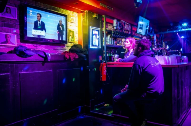 Des clients et salariés d'un bar regardent la retransmission de la conférence de presse du Premier ministre néerlandais Mark Rutte annonçant de nouvelles restrictions sanitaires, le 12 novembre 2021 à Eindhoven