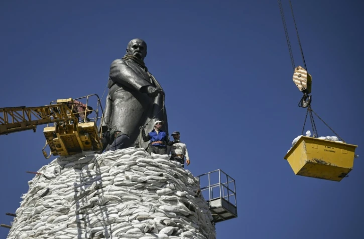 Des employés municipaux disposent des sacs de sable autour d'un momument pour le protéger des bombardements russes, le 26 mars 2022 à Kharkiv (est de l'Ukraine)