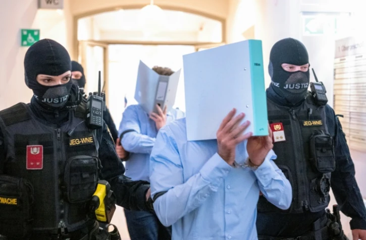 Des prévenus cachent leurs visages derrière un dossier, escortés par des policiers vers la salle d'audience du tribunal de Wiener Neustadt, le 28 mai 2026 en Atriche, lors du procès pour un complot contre un concert de la star américaine Taylor Swift à Vienne