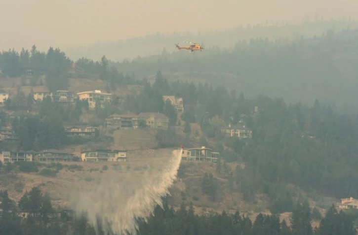 Un hélicoptère lâche de l'eau pour lutter contre les flammes à West Kelowna en Colombie-Britannique, le 19 août 2023