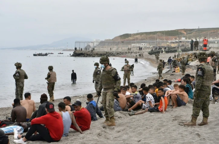 Des migrants, parmi lesquels des mineurs, arrivés à la nage depuis le Maroc sur l'enclave espagnole de Ceuta, se reposent devant des soldats espagnols montant la garde le 18 mai 2021