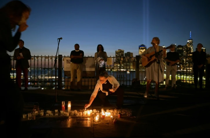 Une femme allume une bougie et une autre joue de la guitare lors d'une veillée interconfessionnelle à Brooklyn Heights avec l'illumination sur le site de Ground Zero en toile de fond, à New York le 11 septembre 2021