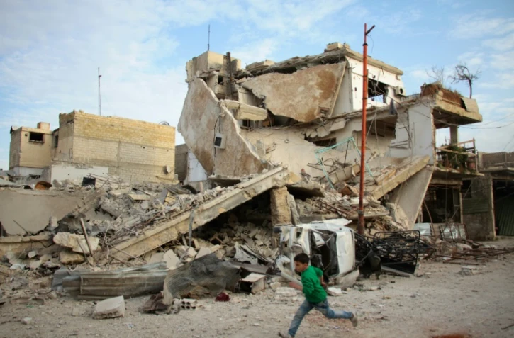 Un garçon syrien court devant un immeuble détruit par des raids du régime dans la ville de Douma, dans le fief rebelle de la Ghouta orientale, le 20 février 2018