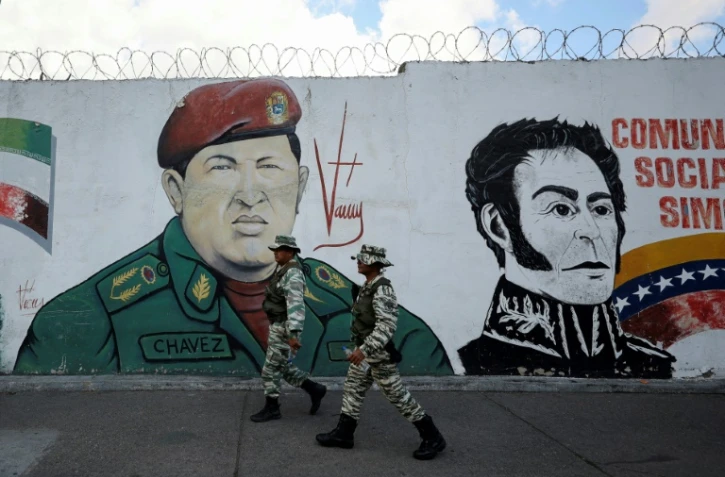 Des miliciens passent devant une fresque murale figurant l'ancien président vénézuélien Hugo Chavez et le libérateur Simon Bolivar, le 7 janvier 2025 à Caracas
