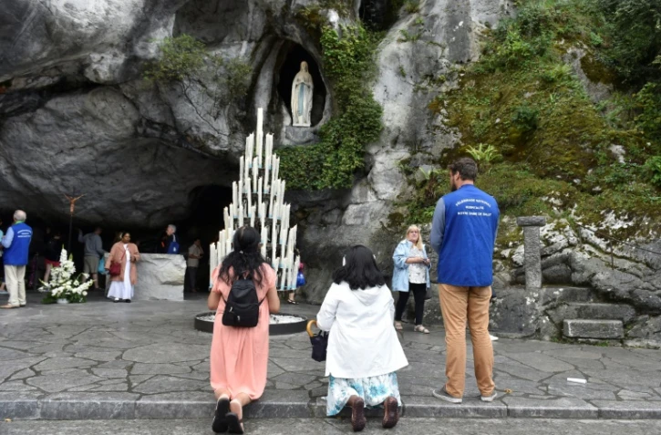 Des pèlerins prient le 15 août 2017 devant la grotte de Massabielle à Lourdes, où Bernadette Soubirous dit avoir vu des apparitions de la Vierge Marie