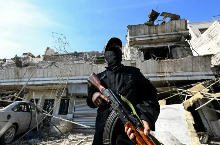 Un membre des forces de sécurité syriennes monte la garde devant un bâtiment détruit par une frappe aérienne israélienne à Damas, le 13 mars 2025