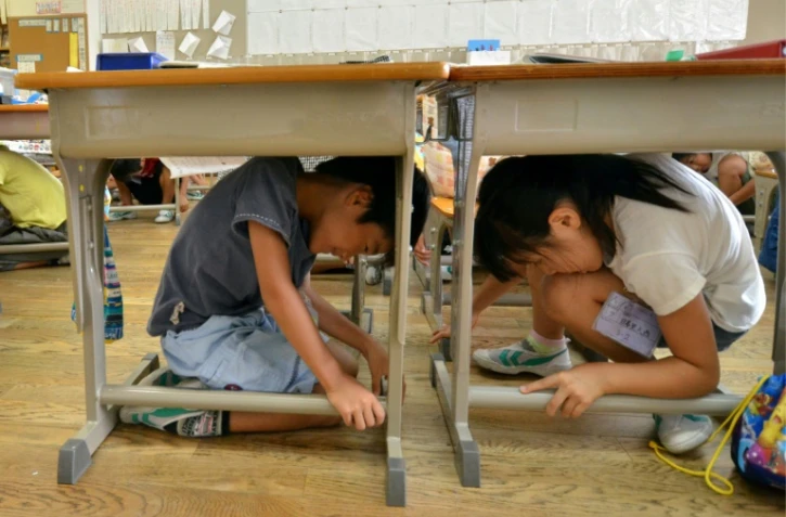 Des écoliers japonais s'abritent sous leur pupitres, lors d'un tremblement de terre, dans une école de Tokyo, le 2 septembre 2013