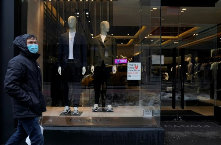 Un homme passe devant la vitrine d'un magasin de vêtements masculins, montrant des mannequins en veste, t-shirt et baskets, sur Madison Avenue, le 15 février 2021
