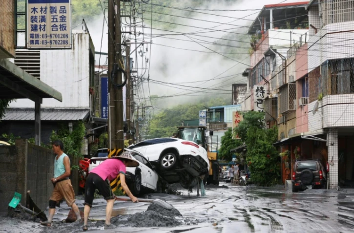 Des habitants nettoient la boue devant chez eux, avec des véhicules renversés en arrière-plan, après la rupture d'une digue au passage du super typhon Ragasa, à Hualien à Taïwan, le 24 septembre 2025