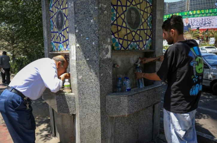 Des passants boivent de l'eau à une fontaine publique dans une rue de Téhéran pendant une vague de chaleur en Iran, le 22 juillet 2025