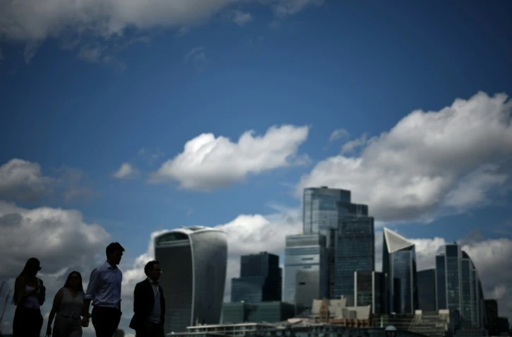 Des passants le long de la rive sud de la Tamise d'où l'on aperçoit le quartier des affaires et financier du centre de Londres, le 14 août 2025