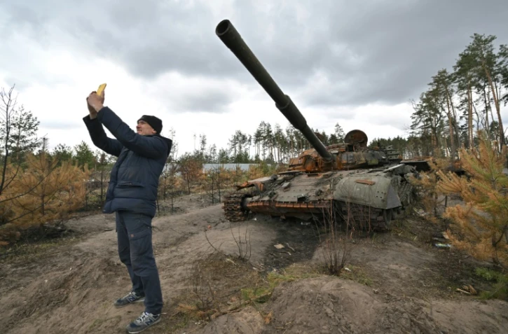 Un homme fait un selfie devant un tank russe détruit dans le village d'Andriivka, dans la région de Kiev, le 17 avril 2022