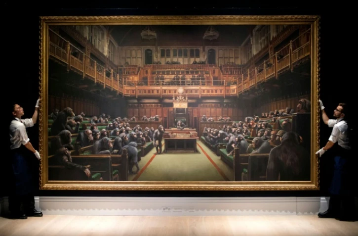 Deux assistants manipulent la toile de Banksy "Devolved Parliament" (Parlement dévolu), le 27 septembre 2019 à Londres