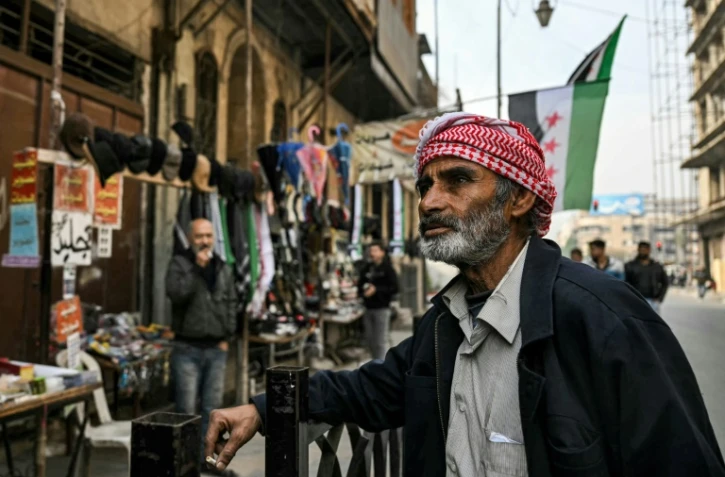 Un passant à proxmité d'échoppes ouvertes dans une rue d'Alep où flotte le drapeau de la rébellion, le 11 décembre 2024.