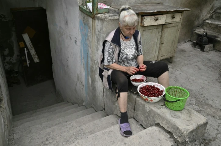Lioudmila, assise devant l'entrée d'un sous-sol servant d'abri, dénoyaute des cerises, le 30 juin 2022 à Seversk, dans la région de Donetsk, en Ukraine