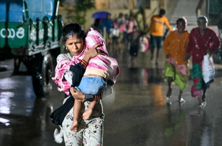 Une femme, un enfant dans les bras, se dirige vers un abri à l'approche du cyclone Arnab, le 27 octobre 2026 à Kakinada, dans l'Etat de l'Andhra Pradesh, en Inde