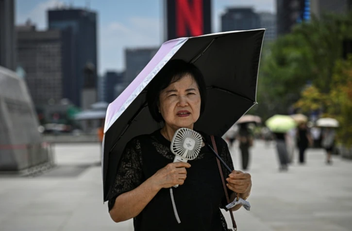 Une femme sous un parapluie avec un ventilateur portatif, le 12 juillet 2026 à Séoul
