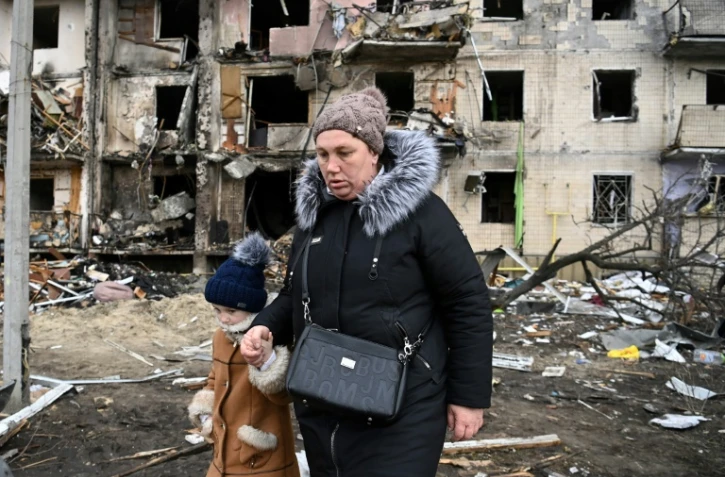 Une femme avec un enfant marche devant un immeuble résidentiel endommagé dans la rue Koshytsa, une banlieue de la de Kiev, le 25 février 2022.