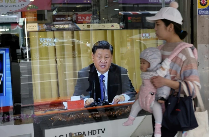Une femme passe avec son bébé à Nouveau Taipei le 2 janvier 2019 devant une télévision montrant le président chinois Xi Jinping qui prononce un discours intransigeant envers Taïwan