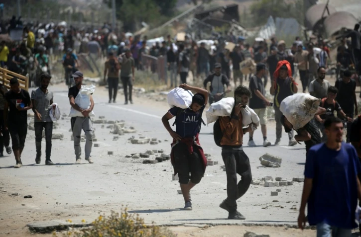 Des Palestiniens transportent des sacs d'aide humanitaire, dans le camp de Nousseirat, dans le centre de la bande de Gaza, le 27 juillet 2025