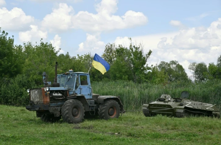 Un fermier ukrainien remorque un blindé de transport de troupes russe abandonné près du village de Mala Rogan, dans la région de Kharkiv, le 28 juillet 2022
