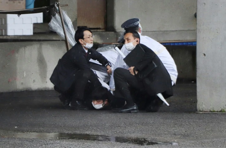 Un homme est immobilisé au sol après avoir lancé un objet ressemblant à une bombe fumigène lors d'un meeting du Premier ministre japonais, à Wakayama, au Japon, le 15 avril 2023