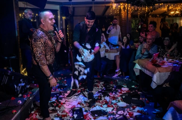 Un chanteur se produit sur la scène d'une taverne pendant qu'un employé brise des assiettes, le 7 janvier 2024 dans la banlieue d'Athènes