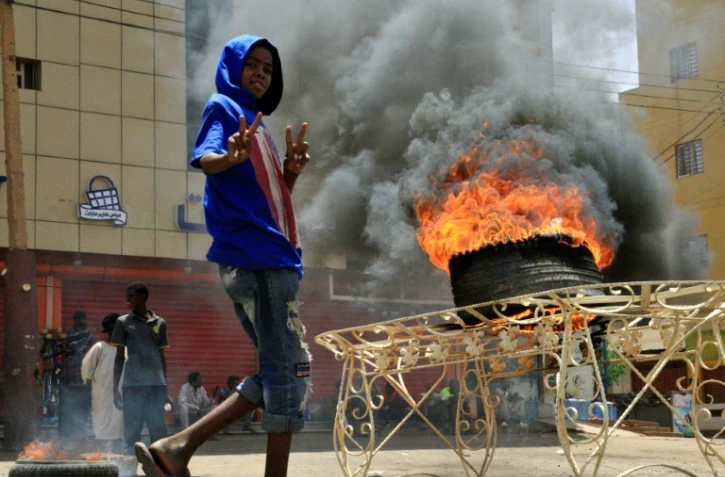 Un manifestant soudanais fait le "V" de la victoire devant un pneu en flammes, le 3 juin 2019 près du siège de l'armée à Khartoum