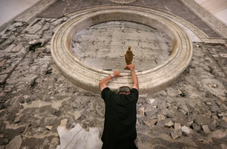 Soutenu à bout de bras, le cardinal Philippe Barbarin escalade le mur de l'église du Saint-Esprit pour y déposer une statue de la Vierge, à Mossoul le 25 juillet 2017