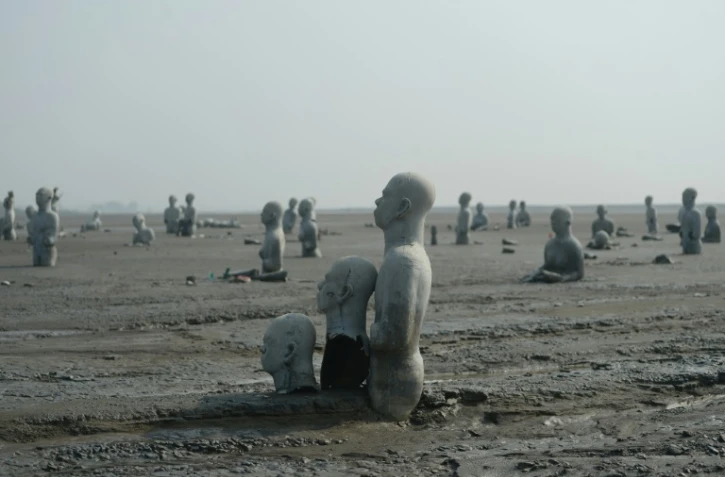 Vue en date du 28 mars 2016 de sculptures de personnes à moitié enterrées dans le volcan de boue qui a surgi de terre le 29 mai 2006 à Sidoarjo