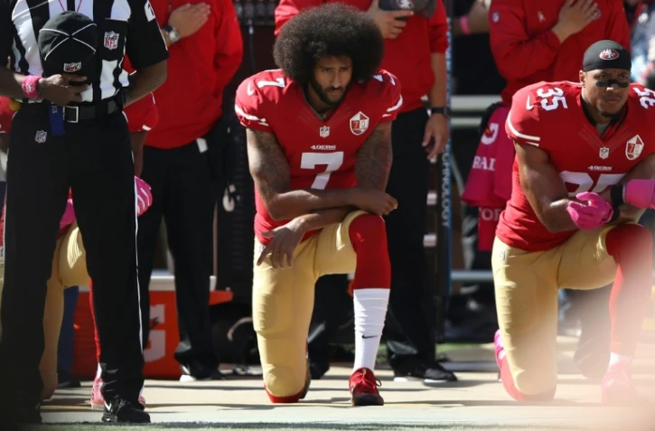 Colin Kaepernick (au centre) s'agenouille avec son partenaire des San Francisco 49ers Eric Reid (droite) pendant l'hymne national avant un match de NFL contre les Tampa Bay Buccaneers le 23 octobre 2016 Ă Santa Clara, en Californie
