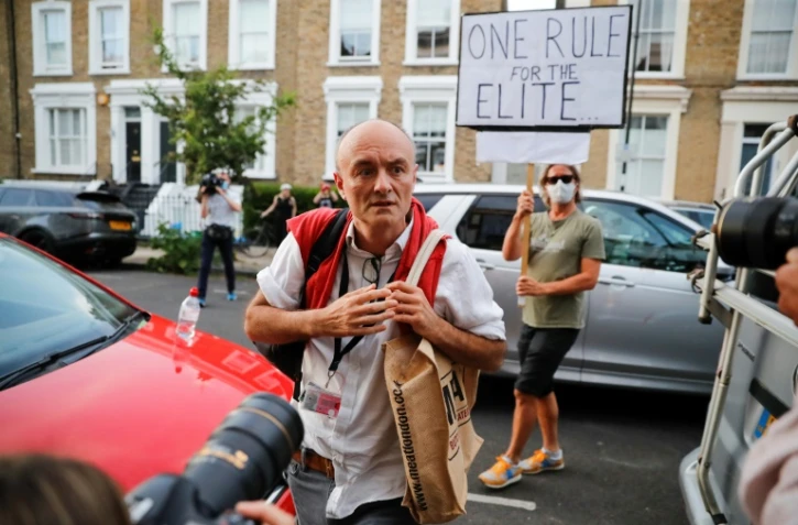 Dominic Cummings, le conseiller du Premier ministre Boris Johnson, à son arrivée chez lui à Londres, le 25 mai 2020, alors qu'une manifestante brandit une pancarte qui dit "Une règle à part pour les élites"