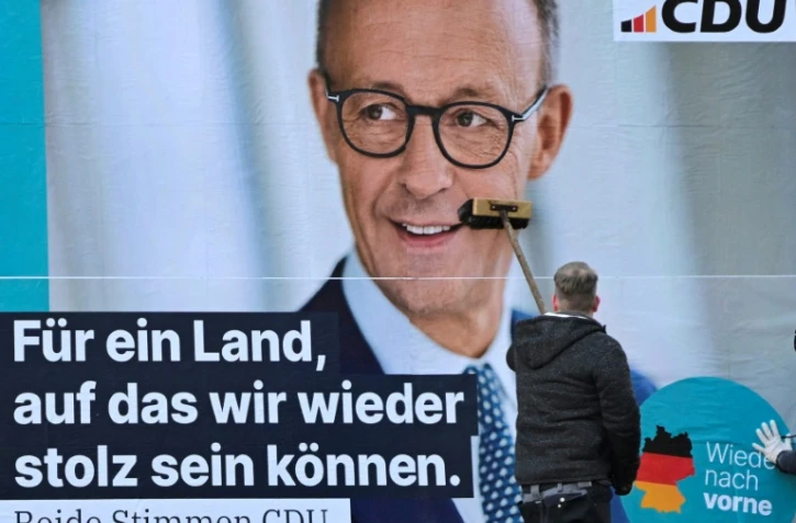 Un homme colle une affiche de Friedrich Merz, leader des conservateurs allemands et favori à la chancellerie, le 13 janvier 2025 à Berlin, en vue des élections législatives anticipées du 23 février