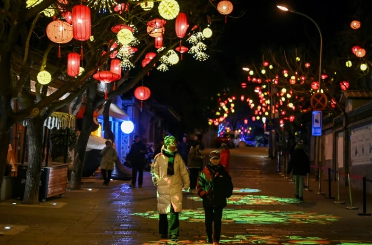 Des piétons dans une rue décorée de lanternes  à la veille de la nouvelle année lunaire du serpent à Pékin, le 28 janvier 2025