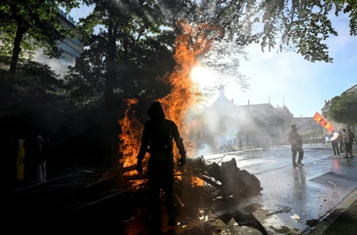 Manifestant devant une poubelle en feu lors d'une manifestation anti-G7 à Genève, le 14 juin 2026