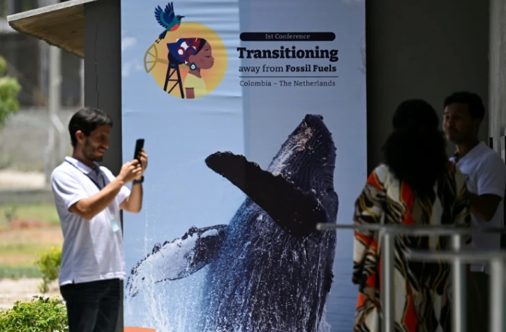 Des personnes prennent une photo devant une affiche de la conférence pour une sortie des énergies fossiles, à Santa Marta, en Colombie, le 26 avril 2026