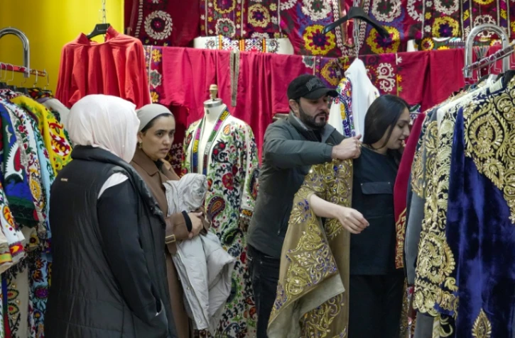 Le styliste Khourched Sattorov présente des vêtements traditionnels à des clientes dans son atelier à Douchanbé, le 2 décembre 2024 au Tadjikistan