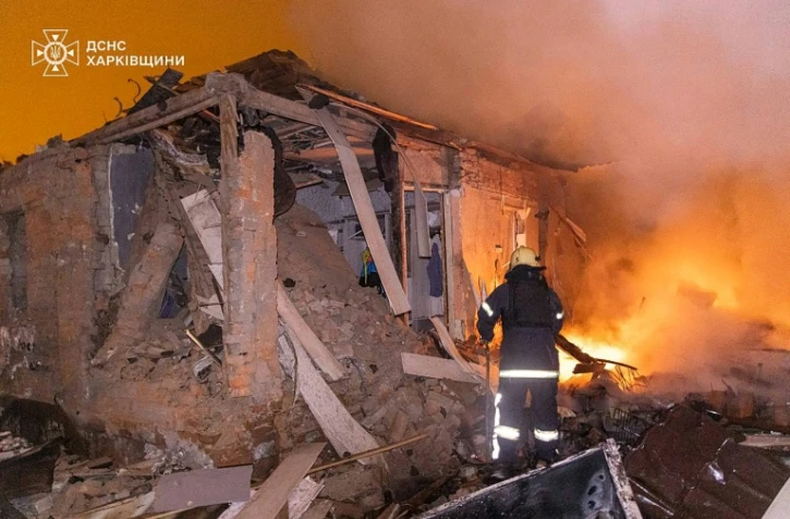 Photo diffusée le 26 février 2026 par le Service ukrainien des situations d'urgence montrant un pompier éteignant un incendie dans une maison endommagée après une attaque russe à Kharkiv