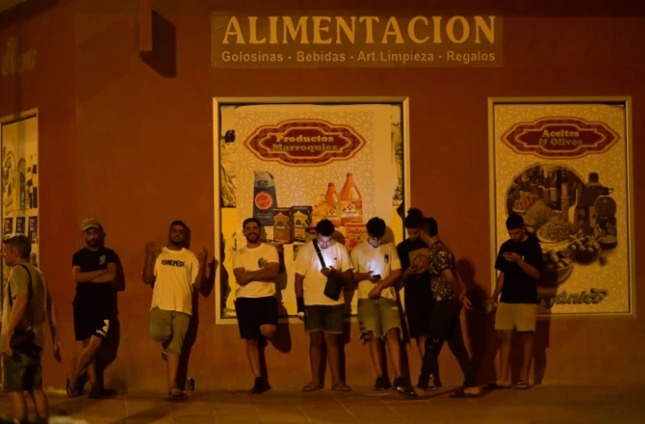Des jeunes hommes consultent leurs téléphones portables à Torre Pacheco (Espagne), le 15 juillet 2025, alors qu'un rassemblement a été appelé par des groupes d'extrême droite après quatre jours de manifestations et de violences anti-migrants